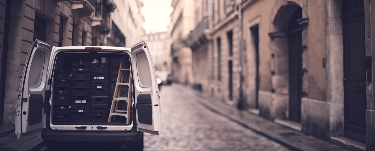 Une camionnette d'artisan ouverte sur ses caisses à outils, garée dans une rue pavée de Lyon au petit matin.